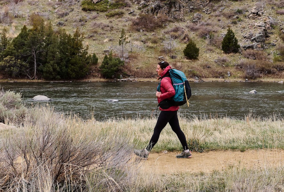 A hiker walks past the camera carrying a full backpacking pack, testing a pair of lone peak shoes