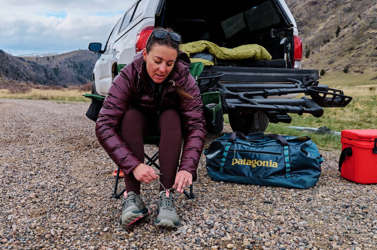 A woman wearing an entirely purple outfit ties a pair of hiking shoes in front of an open truck bed