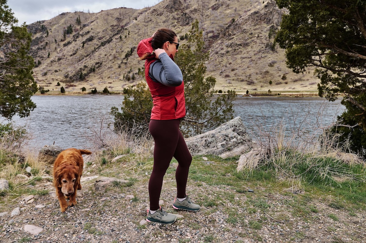 A hiker pulls on the hood of a vest by the river