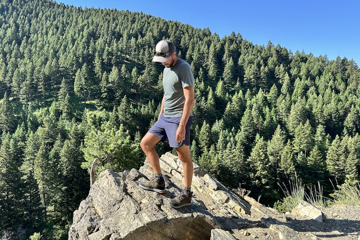 A man stands on a rock in front of trees testing a pair of hiking boots