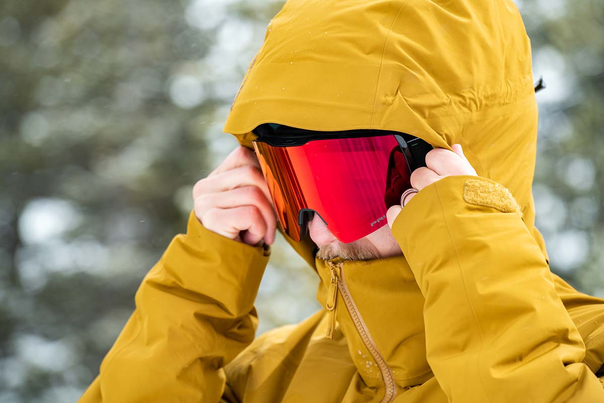A skiier fits the jacket hood to his face, by zipping up the collar and cinching the sides.