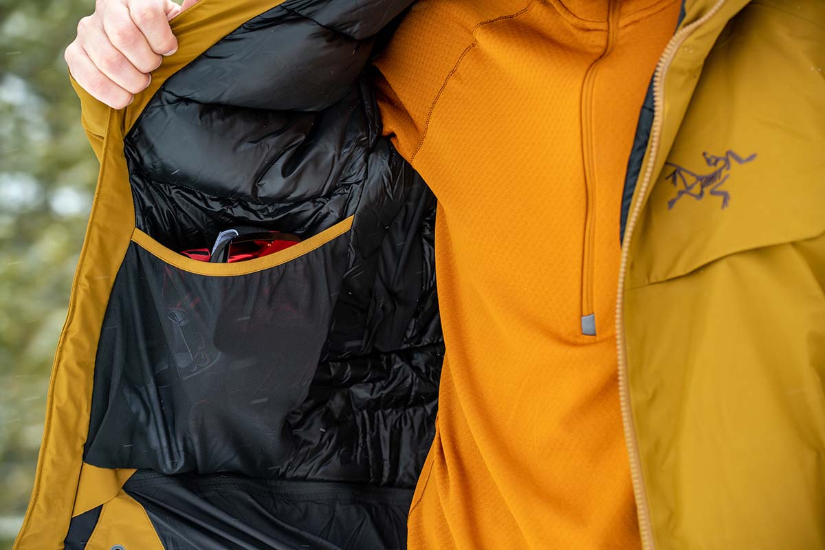 A tester holds the Macai jacket open to show the depth of the right interior mesh pocket. 