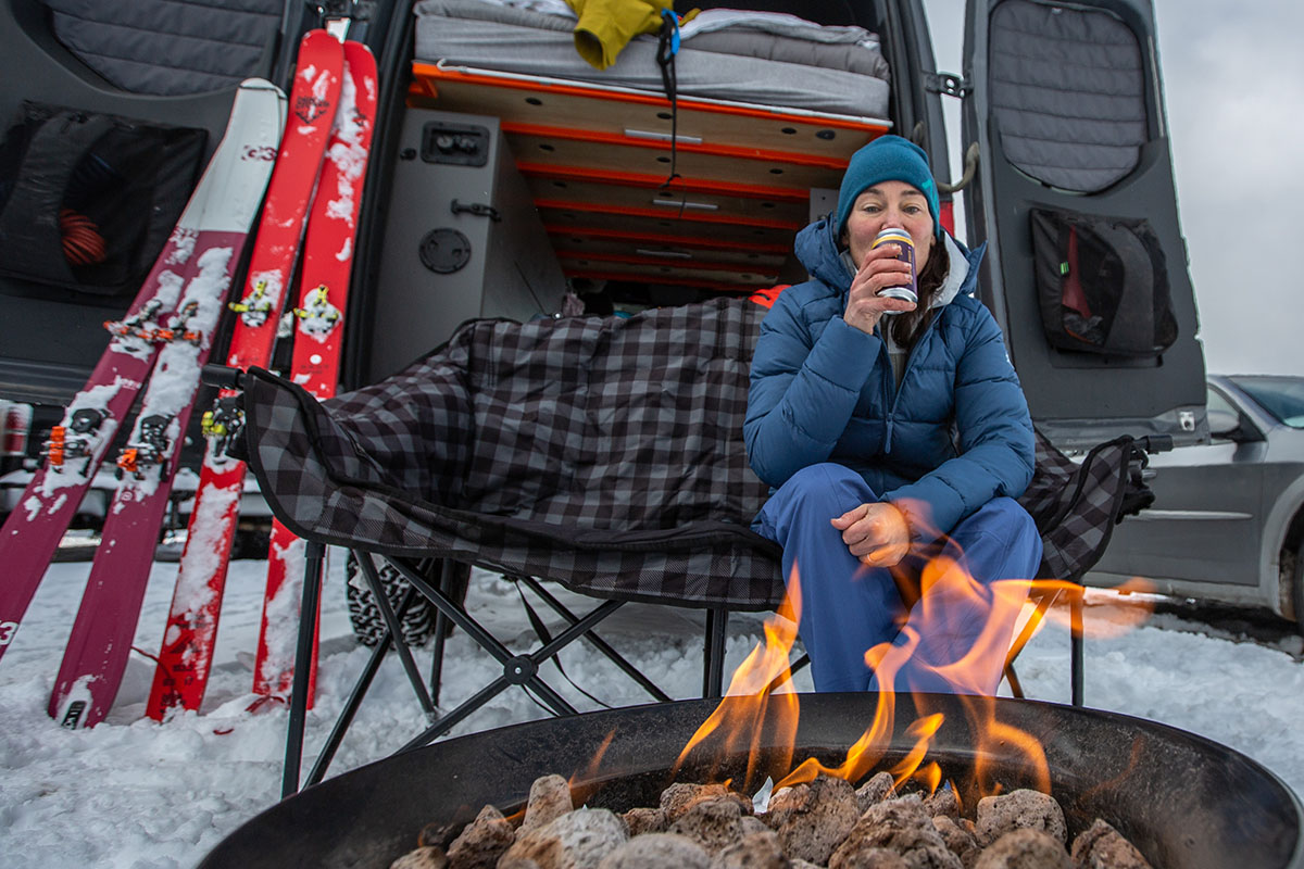 A skiier tailgates by a fire after a fun day, and stays warm in her Thorium coat.