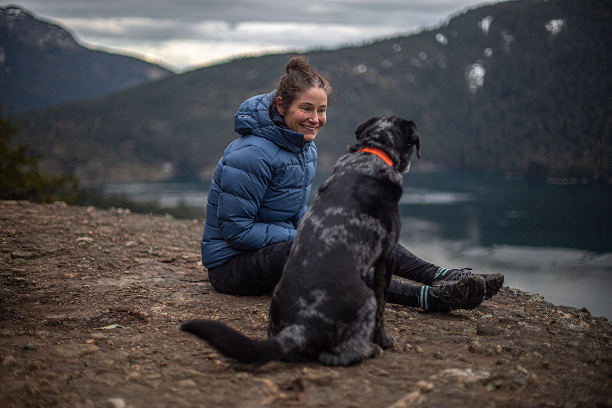 A tester takes a break and sits with her dog on a cloudy day hike.