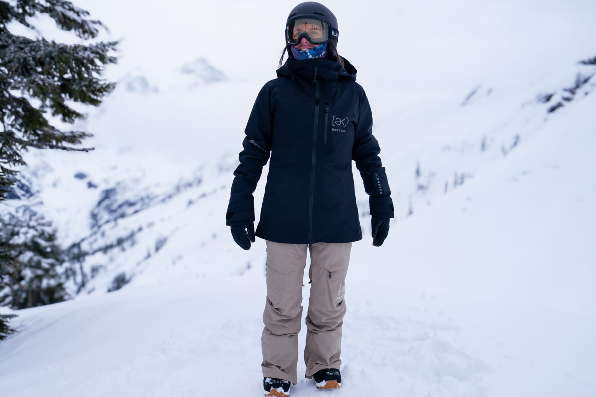 A woman standing in the snow wearing snowboard pants