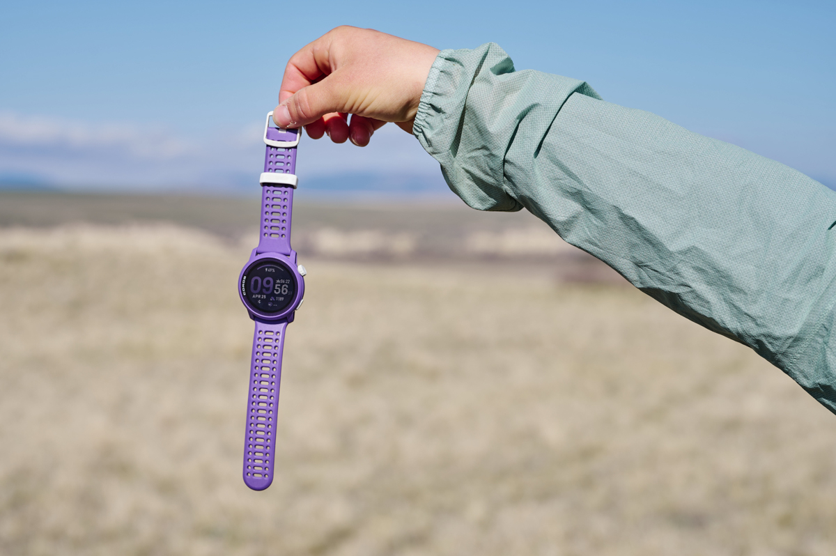A hand holding a purple GPS watching out by the band in front of a grassy field