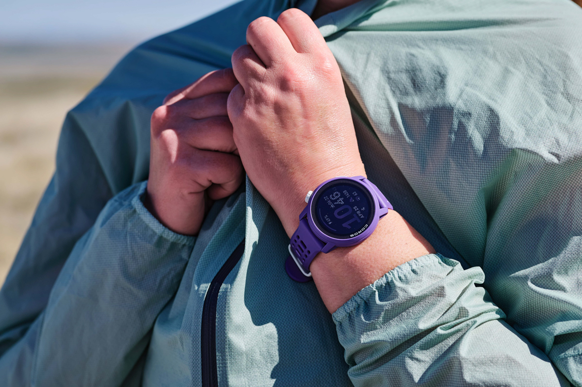 A purple GPS watch on a wrist while hand zips up blue jacket
