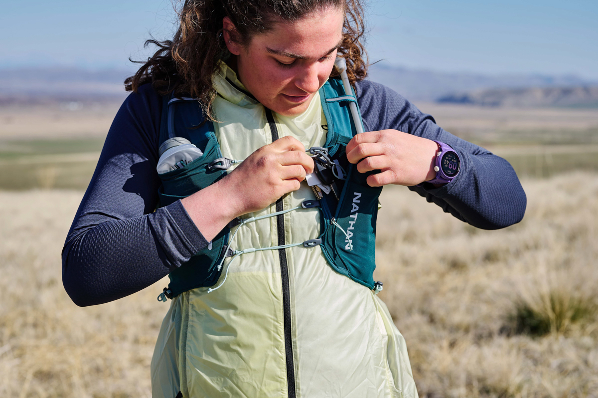 A woman accessing her running vest while wearing a purple GPS watch