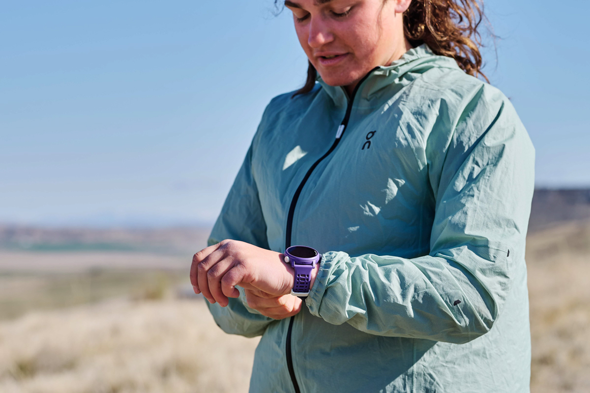 A woman looking down while strapping a puple GPS watch to her wrist