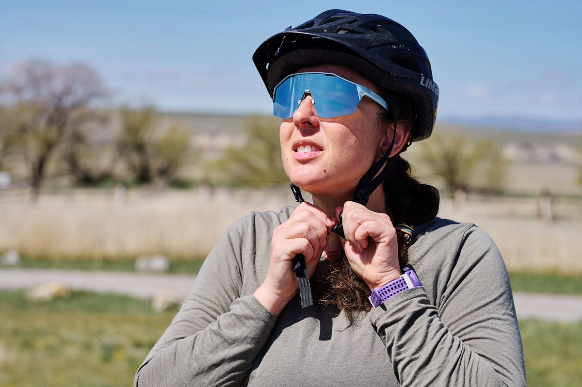 A woman putting on a bike helmet while wearing a purple fitness watch