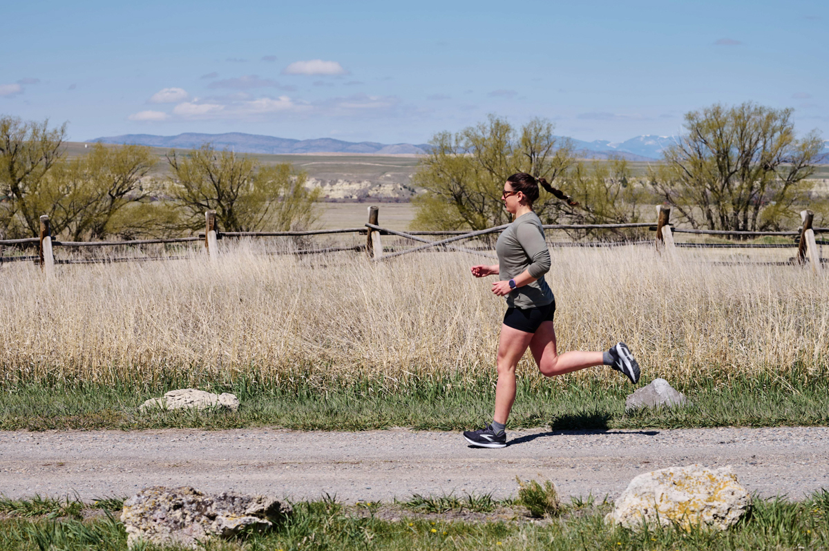 A woman running on a dirt road while wearing a purple fitness watch