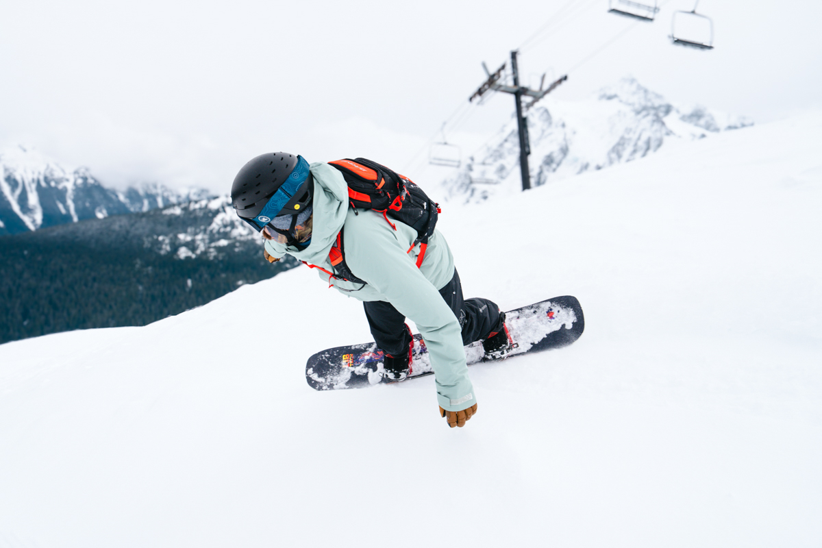 A man snowboarding downhill quickly while wearing ared ski backpack