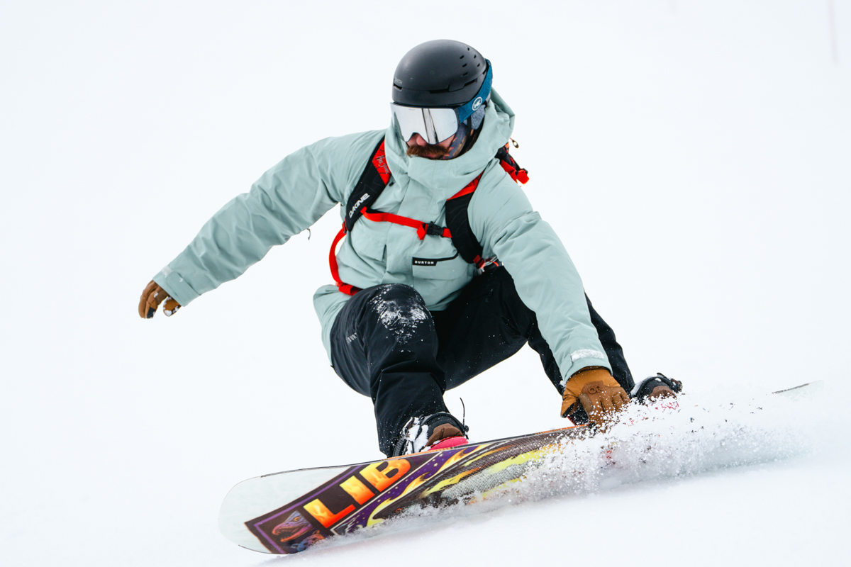 A man snowboarding quickly down a slope while wearing a red ski backpack