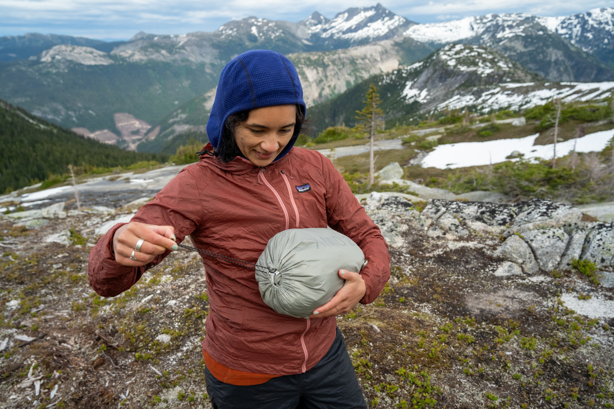 A woman carrying a tent packed down in a stuff sack