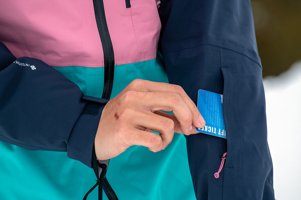 A closeup of a ski pass being placed into the forearm sleeve on the Flylow Lucy jacket
