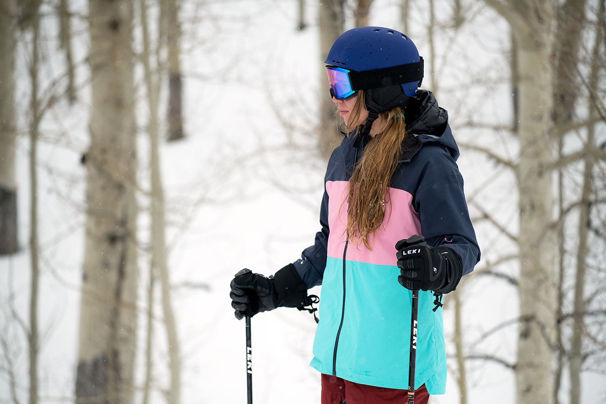 A woman stands among the trees with ski poles
