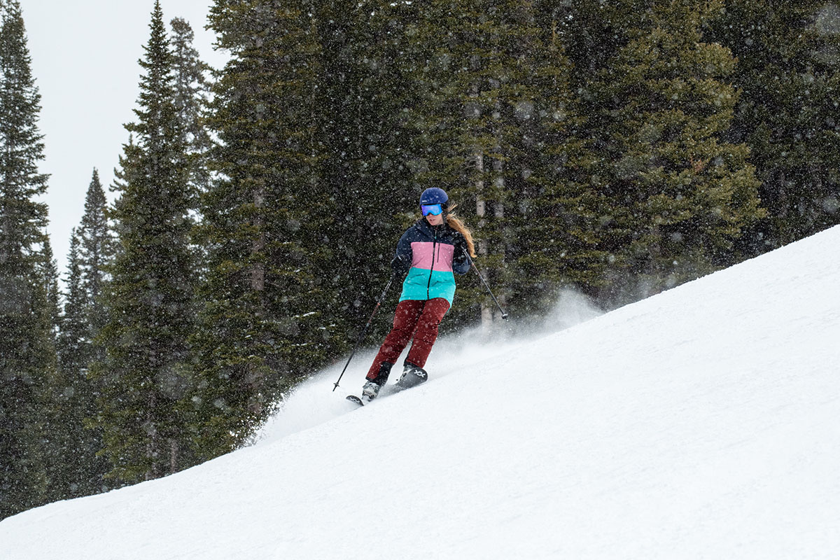 A woman skis through powder and snow amid pine trees