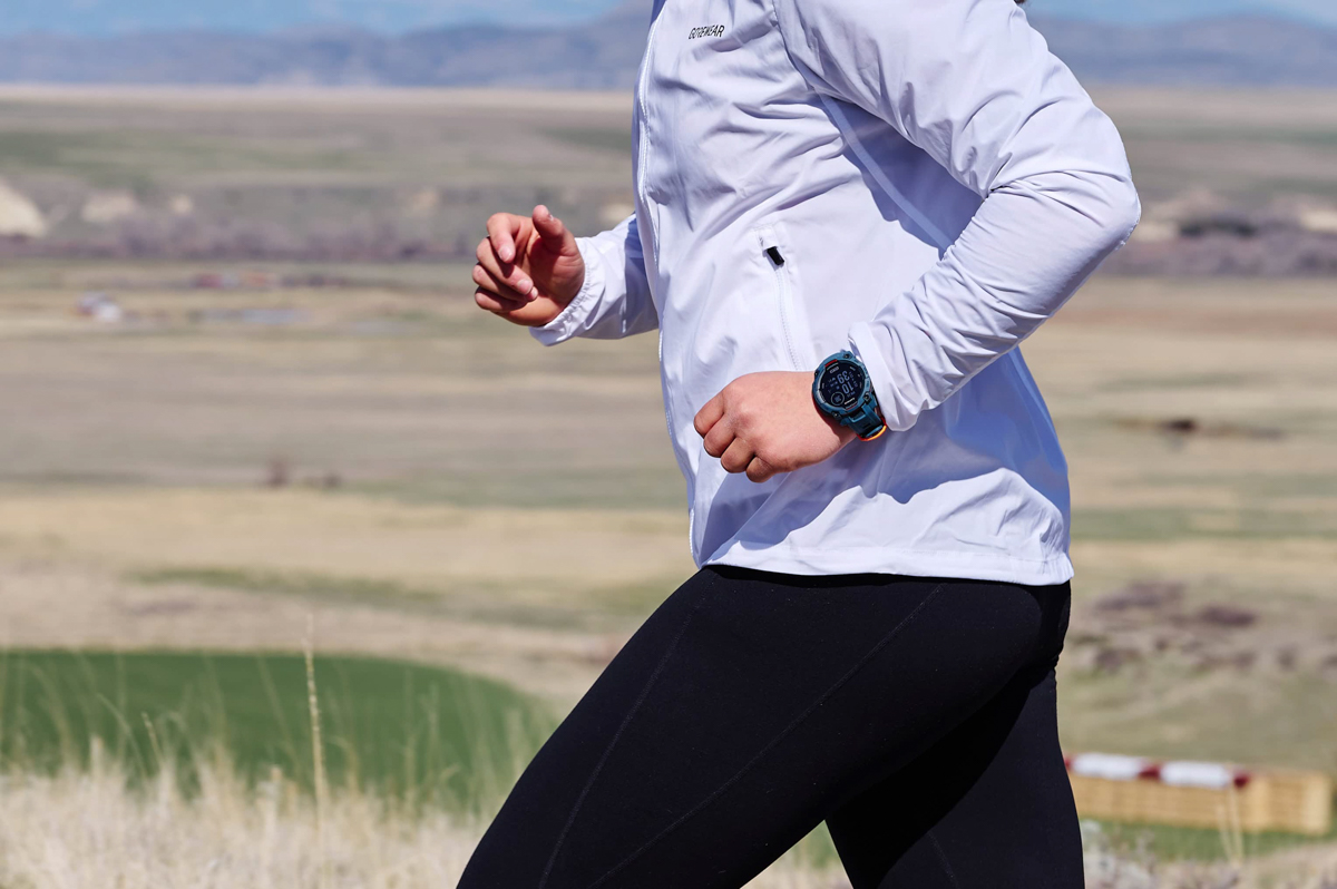 A close up of a woman trail running while wearing a blue GPS watch