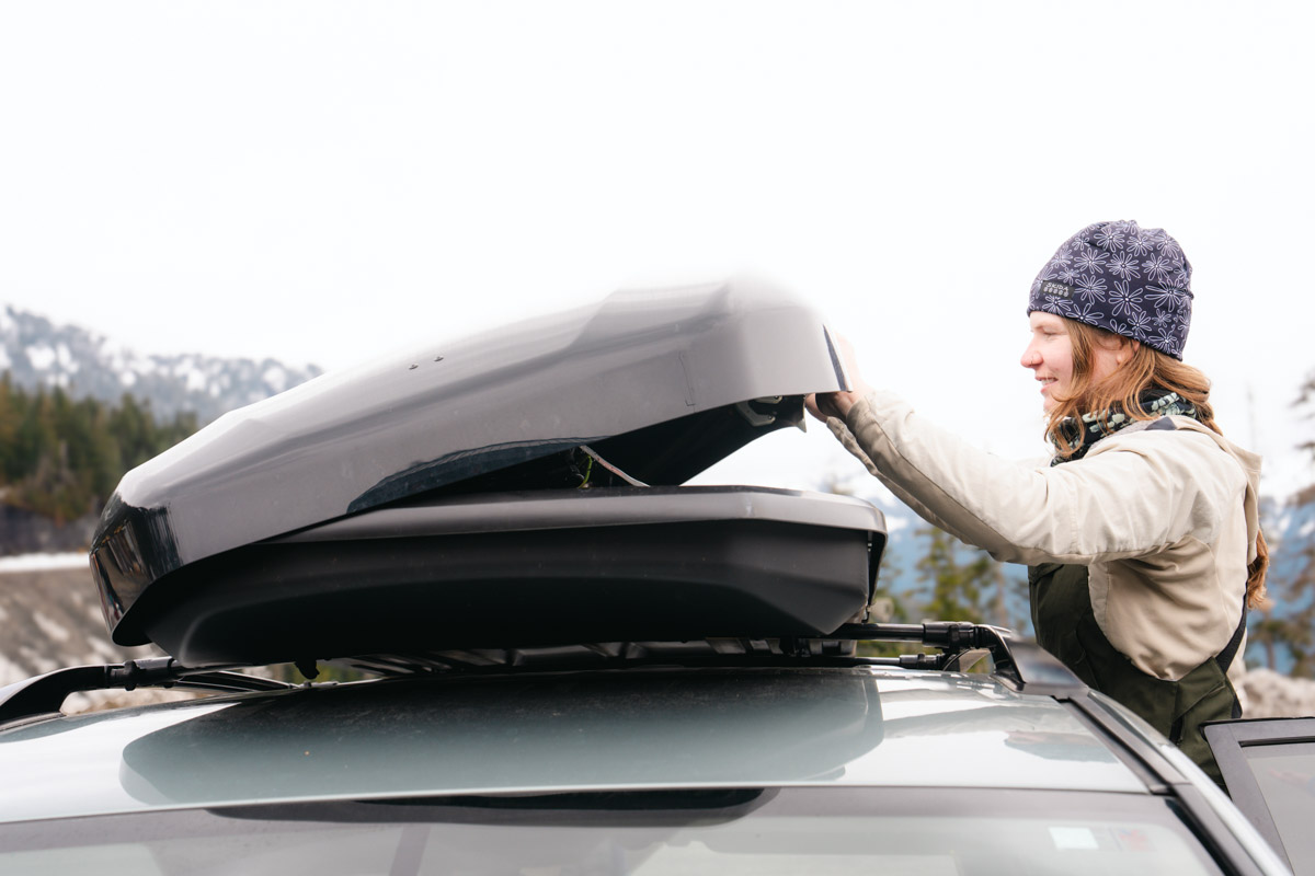 A smiling woman opens a roof box on top of her car