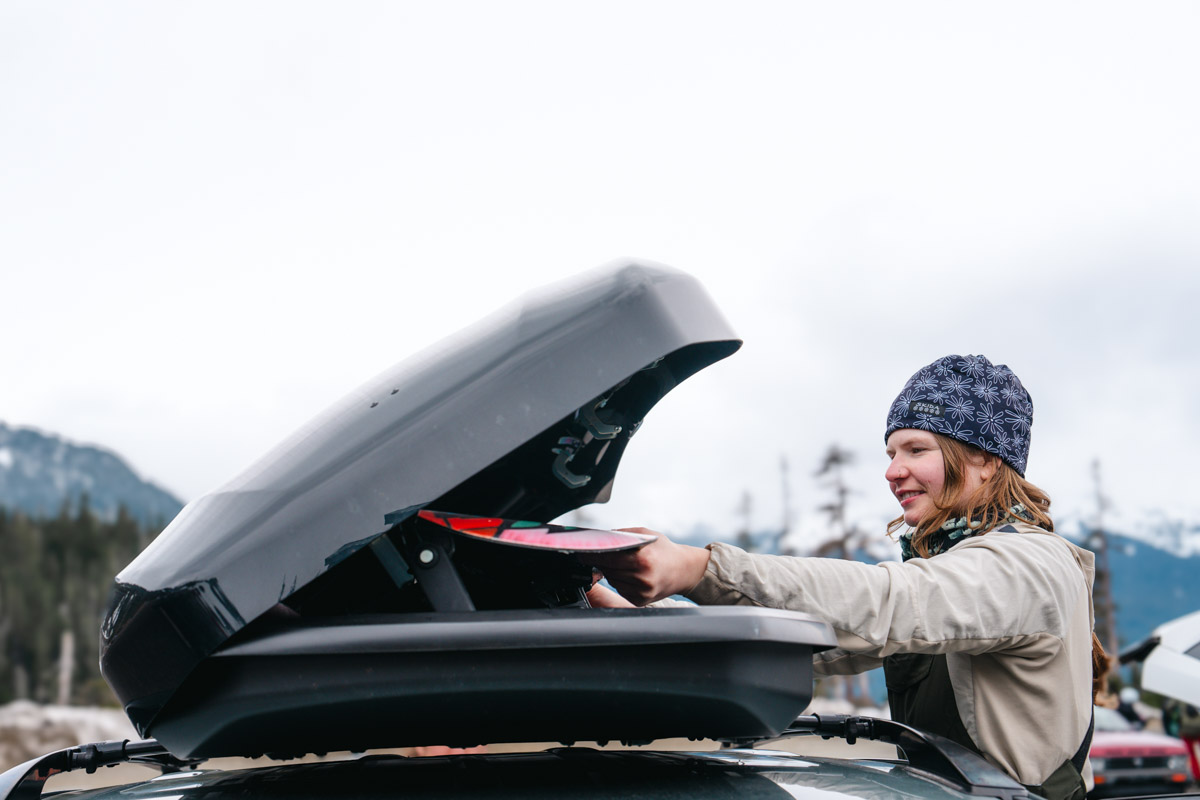 A woman pulls a snowboard out of the Inno Wedge 660 roof box
