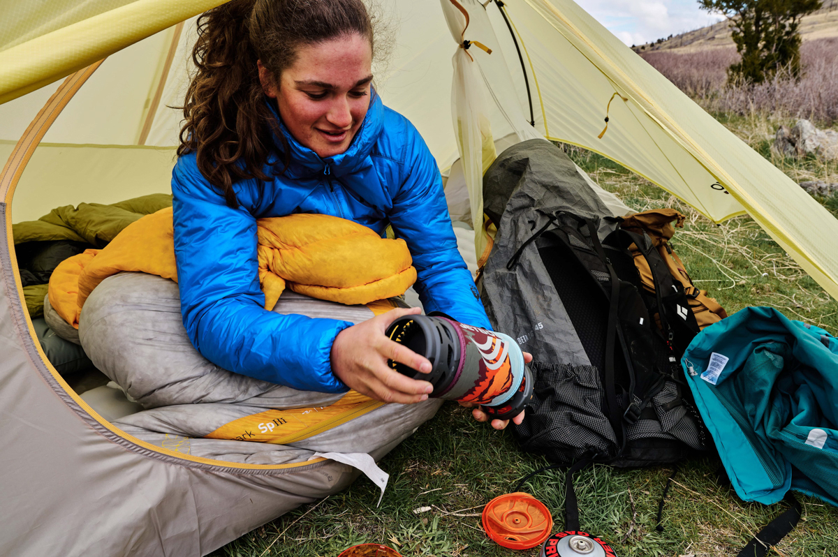 A woman disassembling a backpacking stove while sitting in a tent