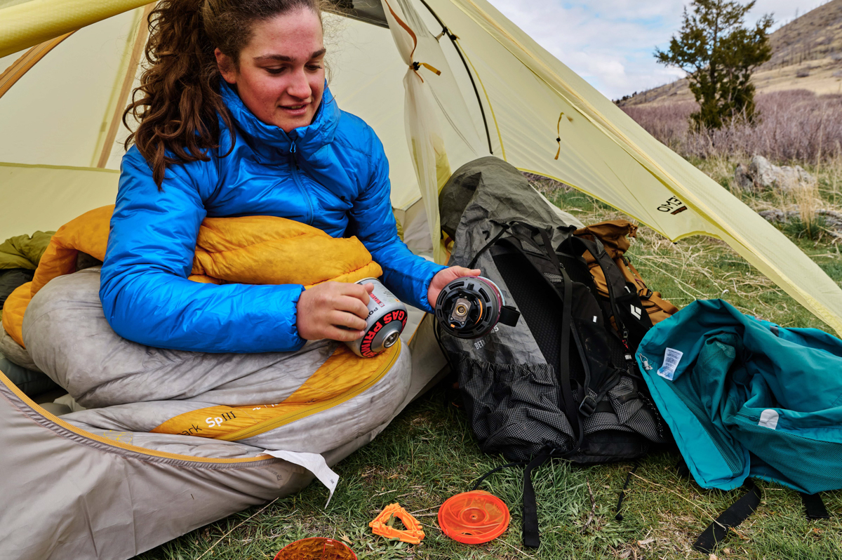 A woman in a tent assembling the parts of a backpacking stove on the ground