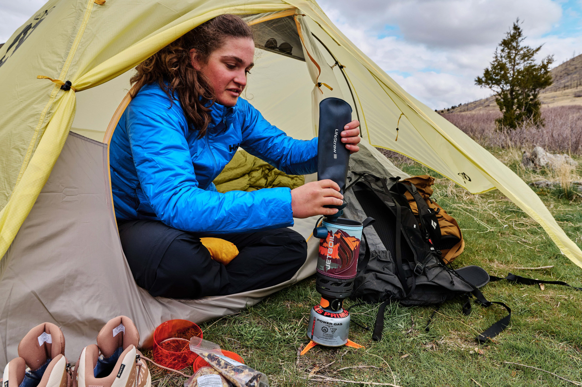 A woman in a tent filtering water into a backpacking stove pot