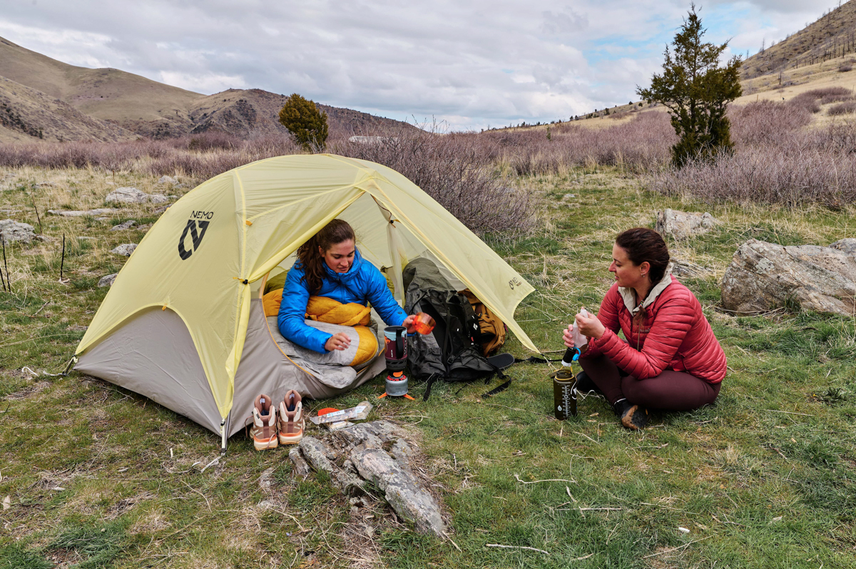 Two women sitting around a tent while boiling water with a backpacking stove