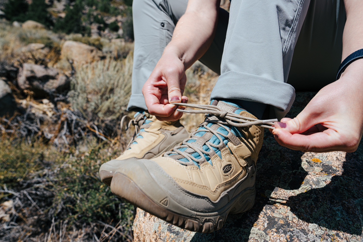 A close up of hands tying a pair of brown leather waterproof boots