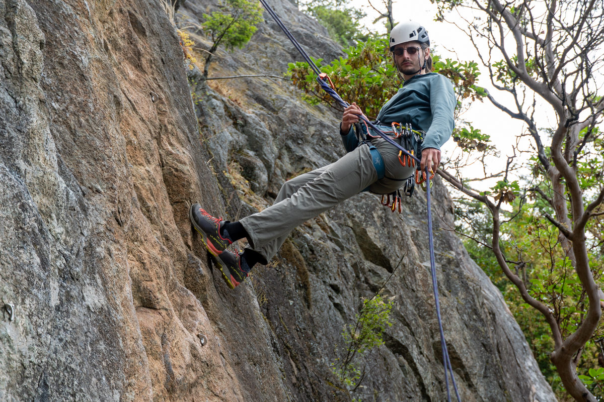 A man rapelling down a rock face while wearing black and red approach shoes
