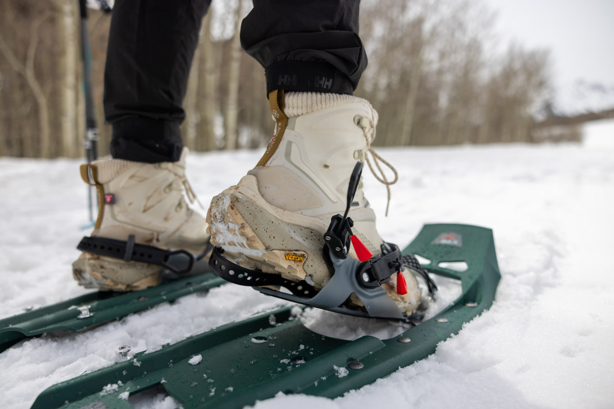 A foot lifting on a pair of green snowshoes