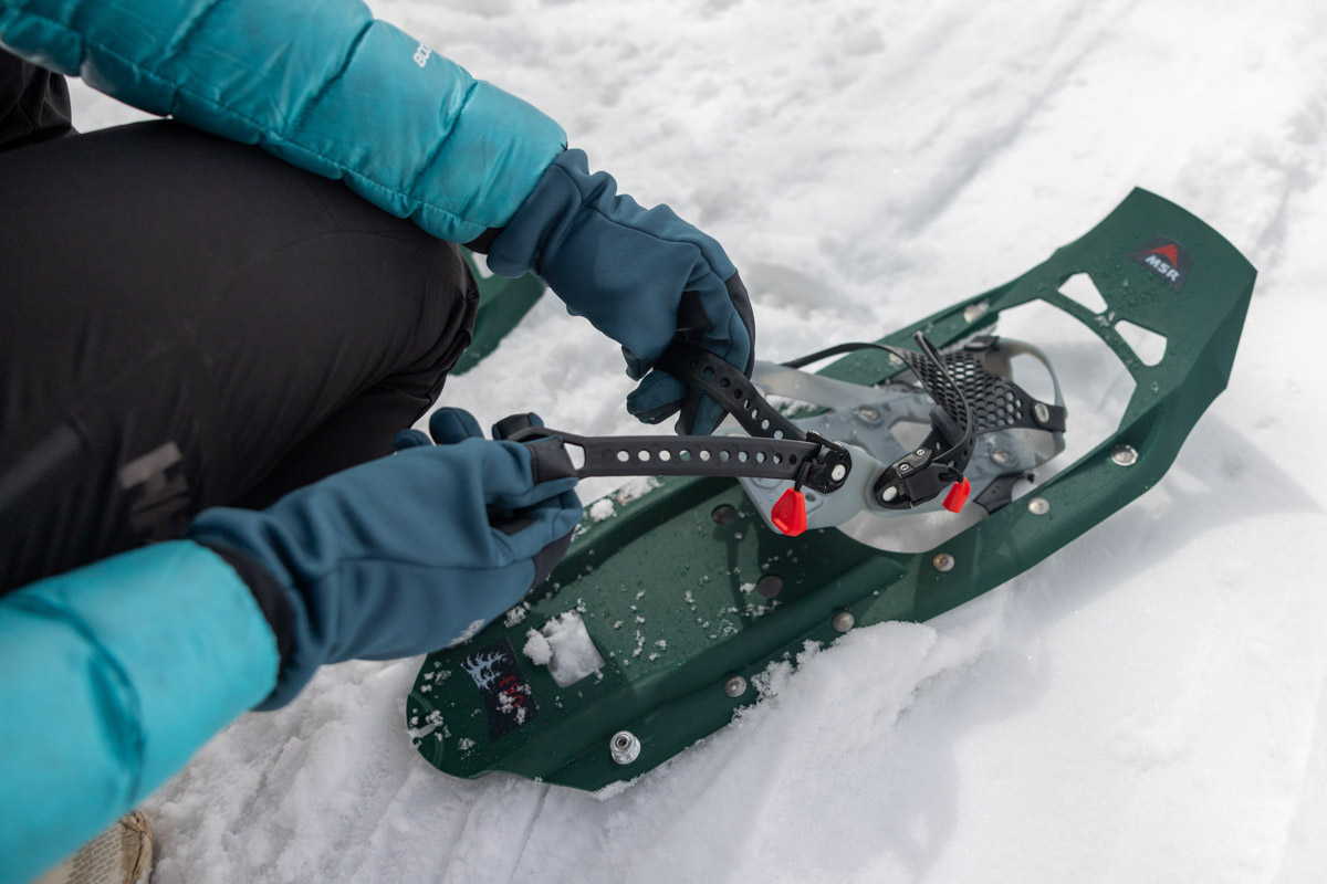 A hand adjusting straps on a pair of snowshoes
