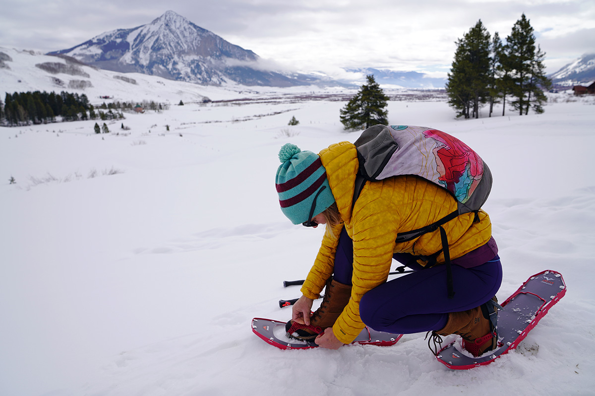 A woman kneeling to adjust binding on snowshoe