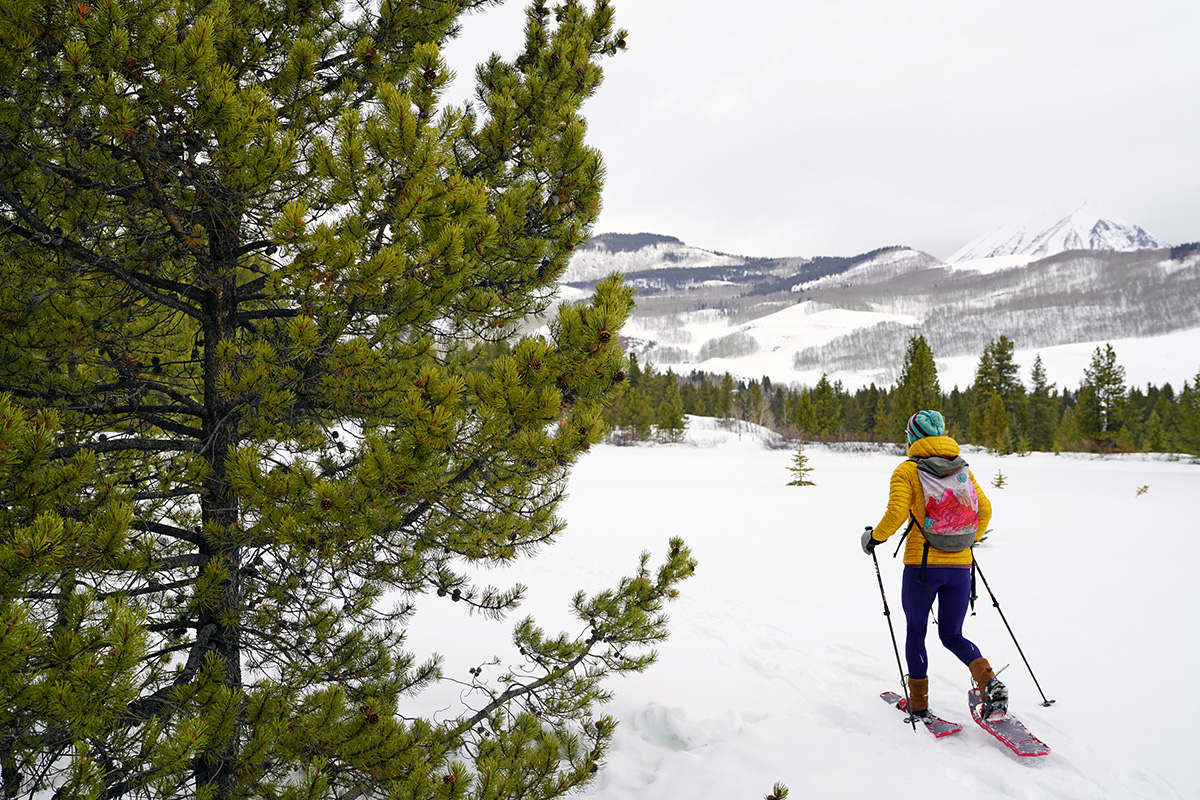 A woman hiking through a snow-filled forest with snowshoes