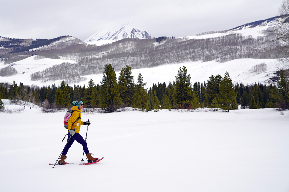 A woman hiking across a snowy meadow in snowshoes