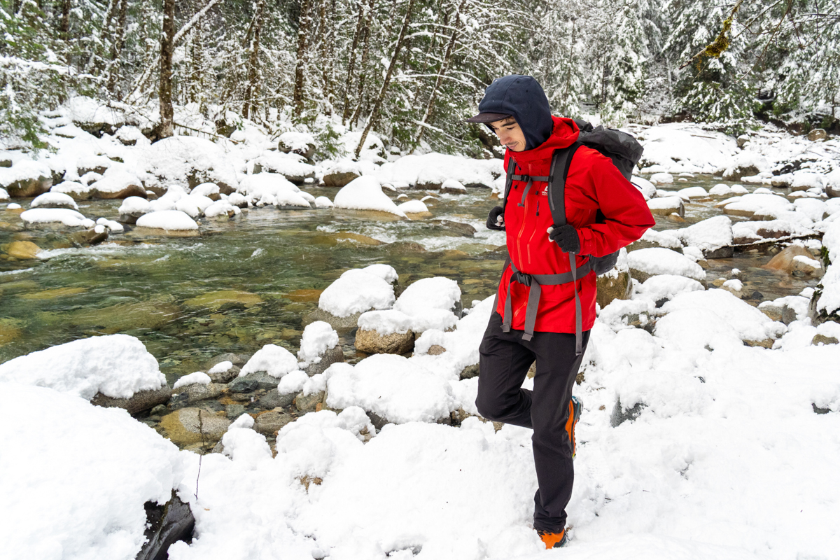 A man hiking in a snowy river lanscape in a red hardshell jacket