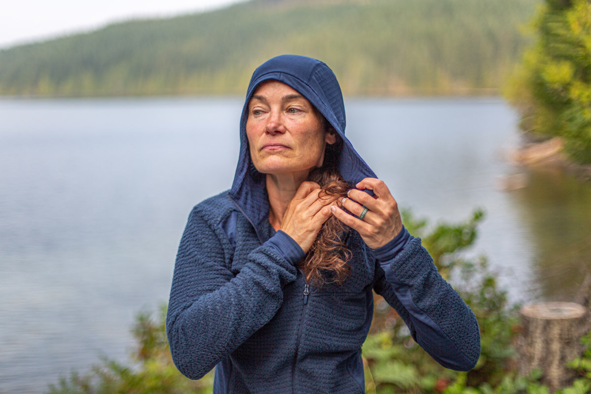 A woman putting on the hood of a blue fleece midlayer