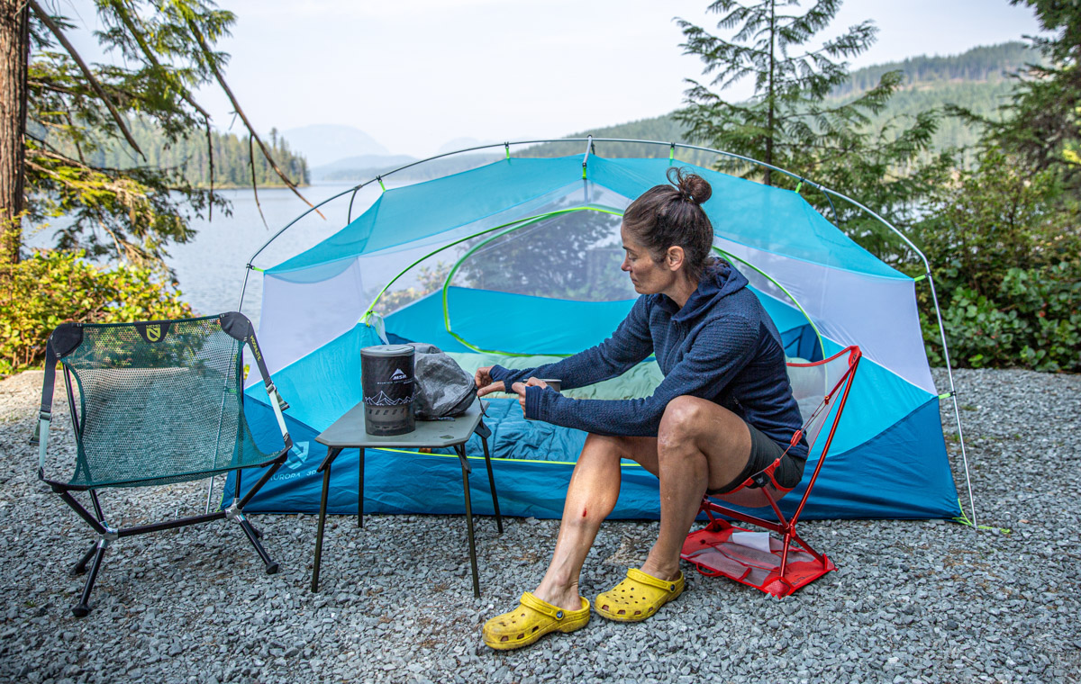 A woman sitting outside of a tent wearing a blue fleece midlayer