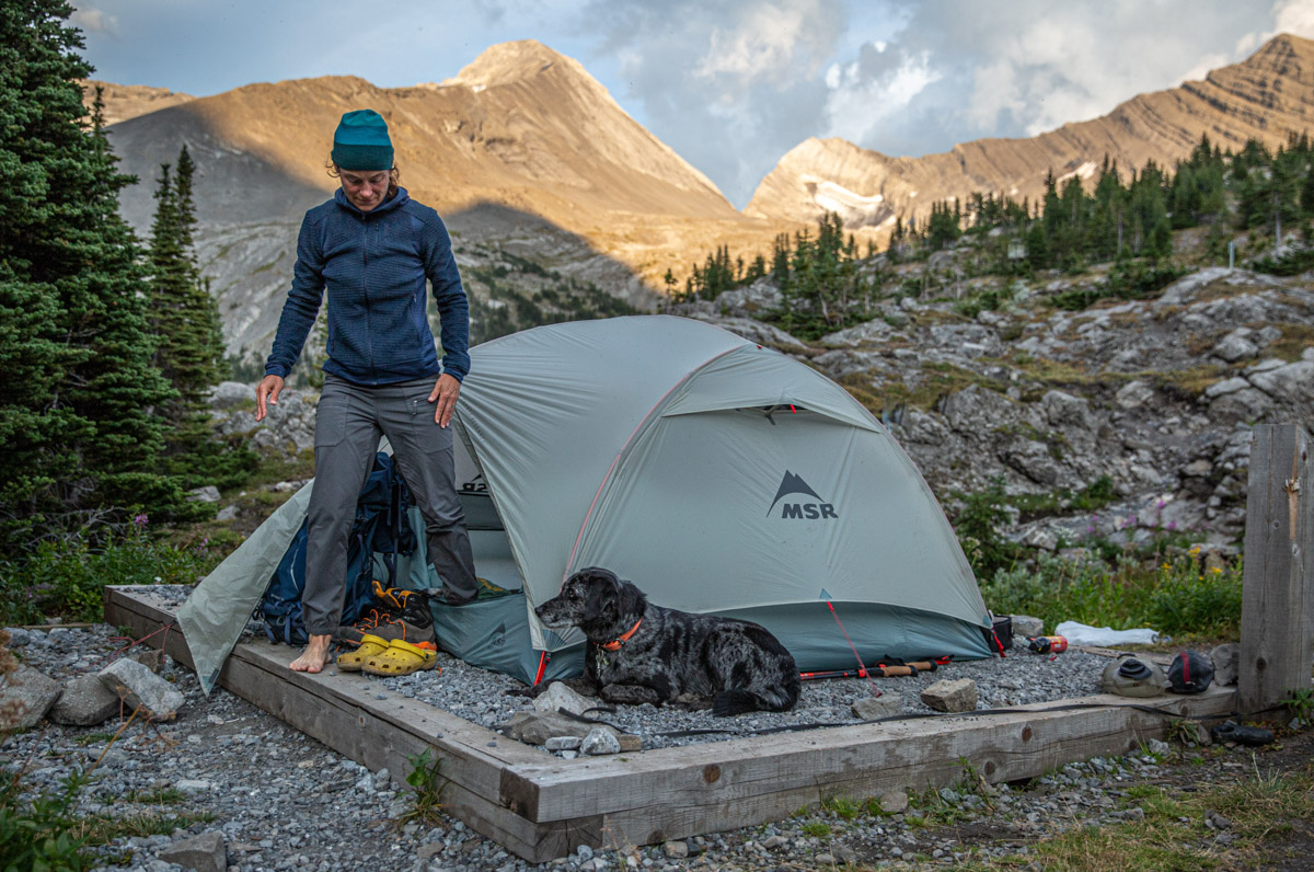 A woman stepping out of a tent wearing a blue fleece midlayer
