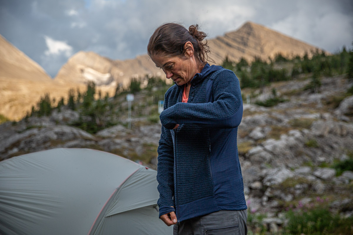 A woman zipping up a blue midlayer in front of a tent