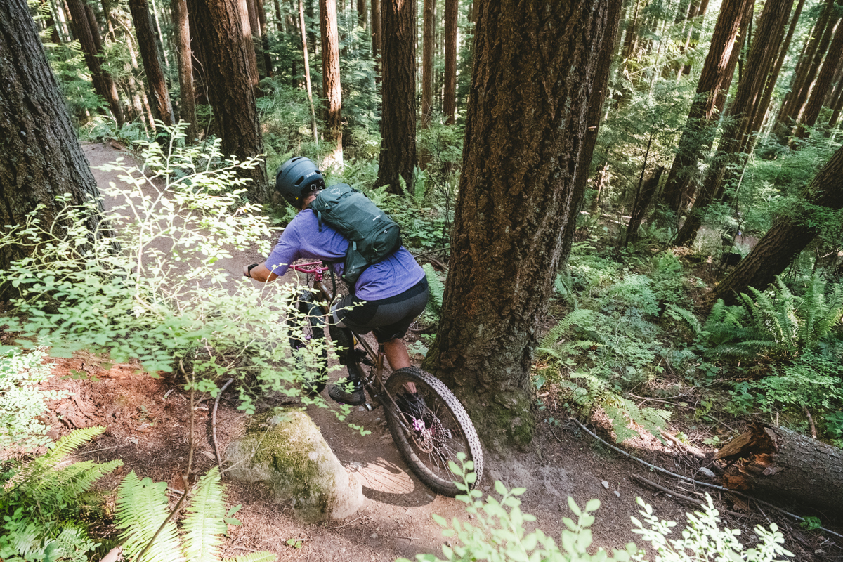 A man riding down a forested trail wearing a mountain bike backpack