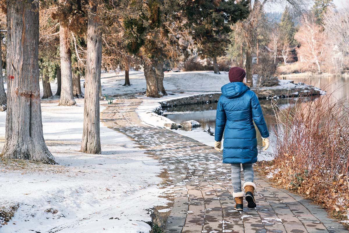 A woman wearing the Patagonia Down With It Parka walks through a snowy park