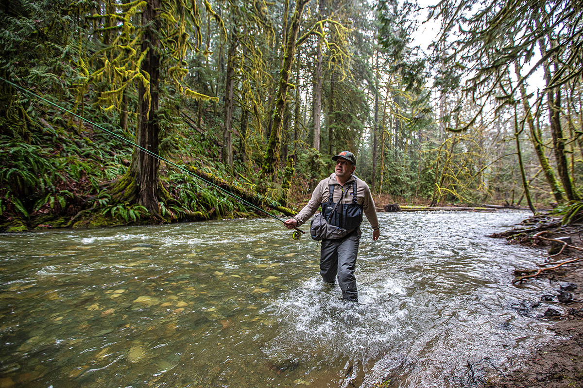 A man stands in a river fly fishing while wearing the  Patagonia TechFace fleece