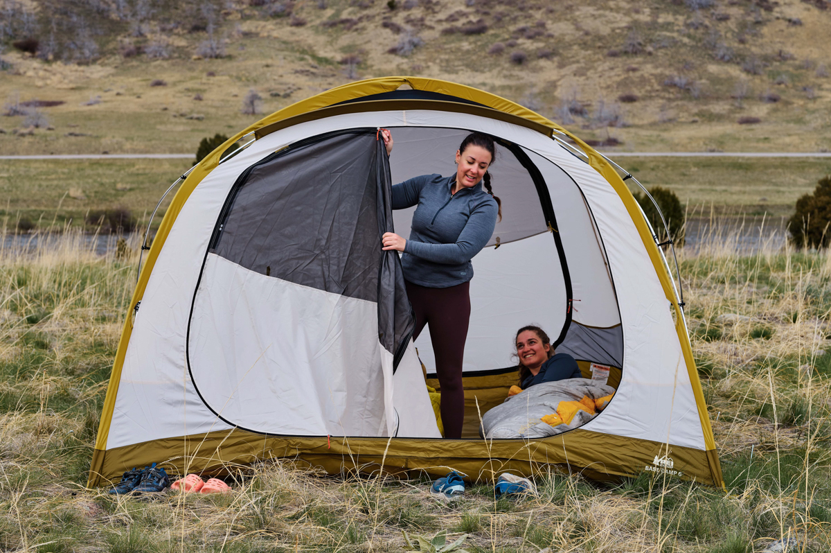 A woman stands in her Base Camp tent and closes the door against rain and weather.