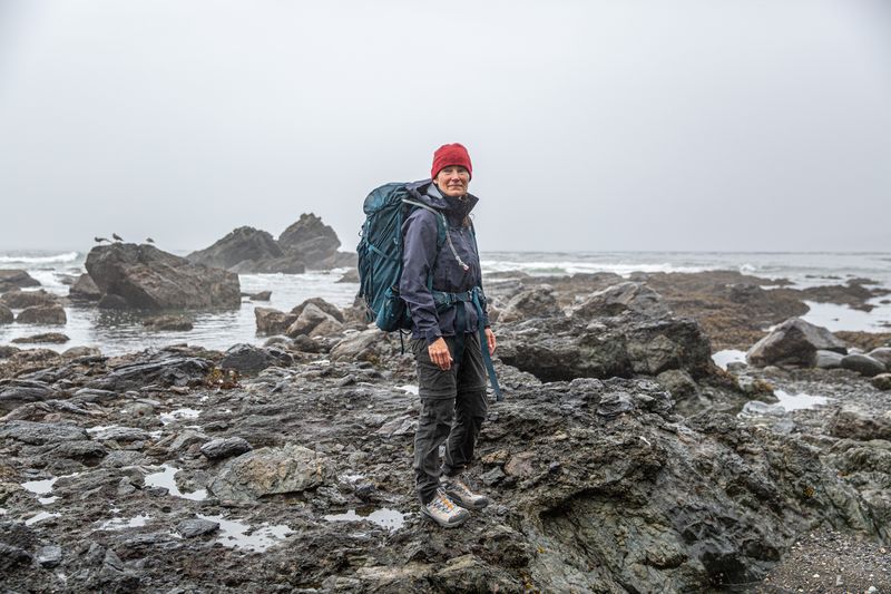a woman stands in the rain on some rocks 