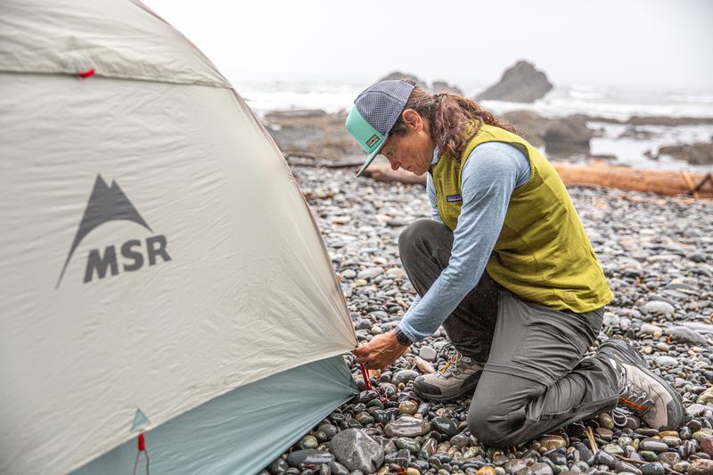 a woman kneels in front of a tent 