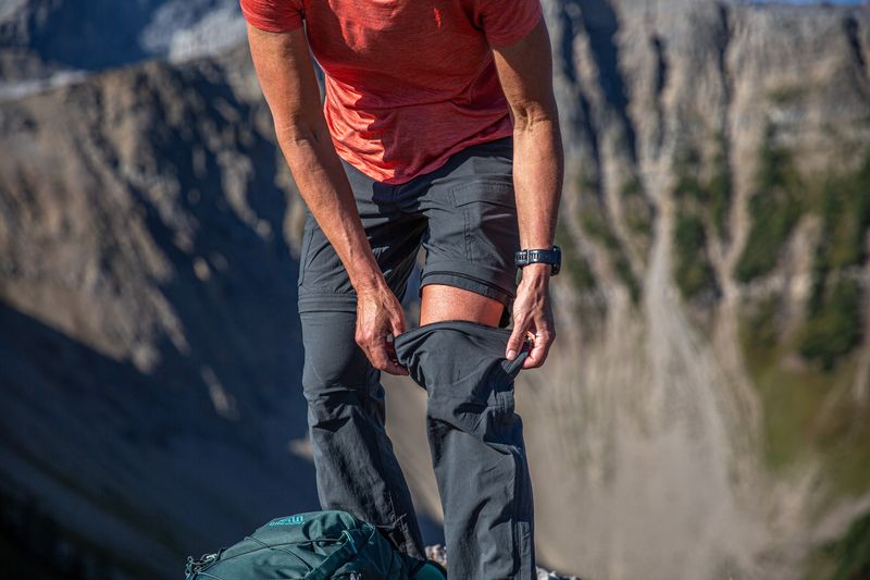 a woman pulls on a the leg of a pair of zip-off pants