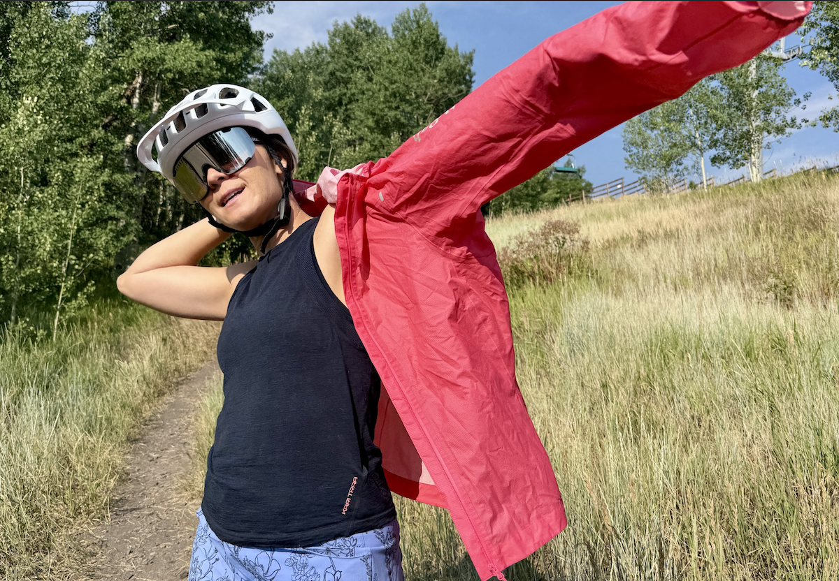 a woman puts on a rain jacket on a bright and sunny day 