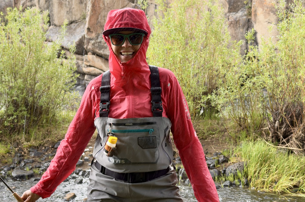 a woman smiles in a rainstorm in waders and a pink jacket