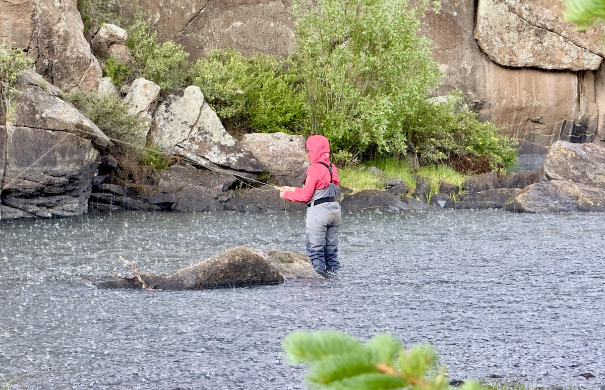 Back view of a woman fly fishing in the rain